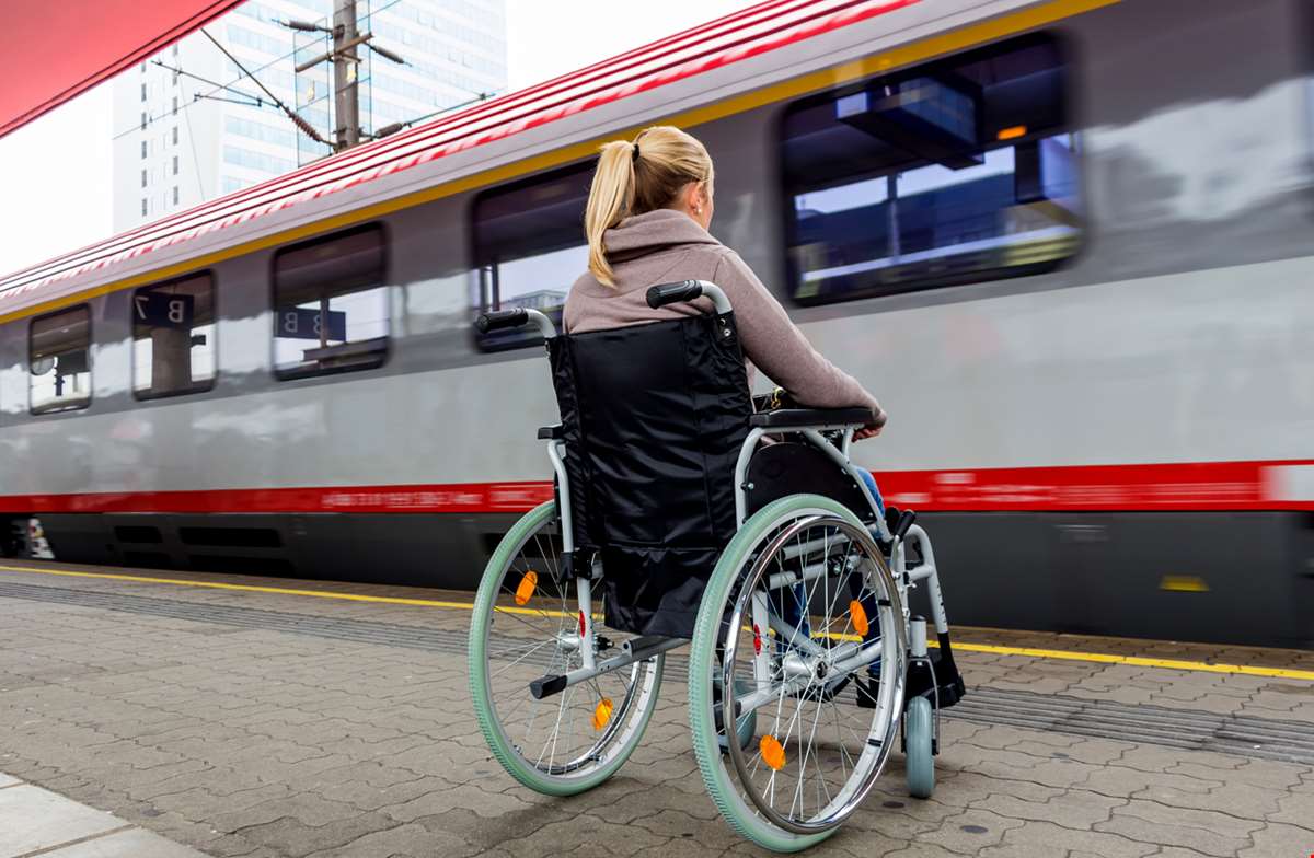 Jente i rullestol venter på toget på jernbanestasjon.